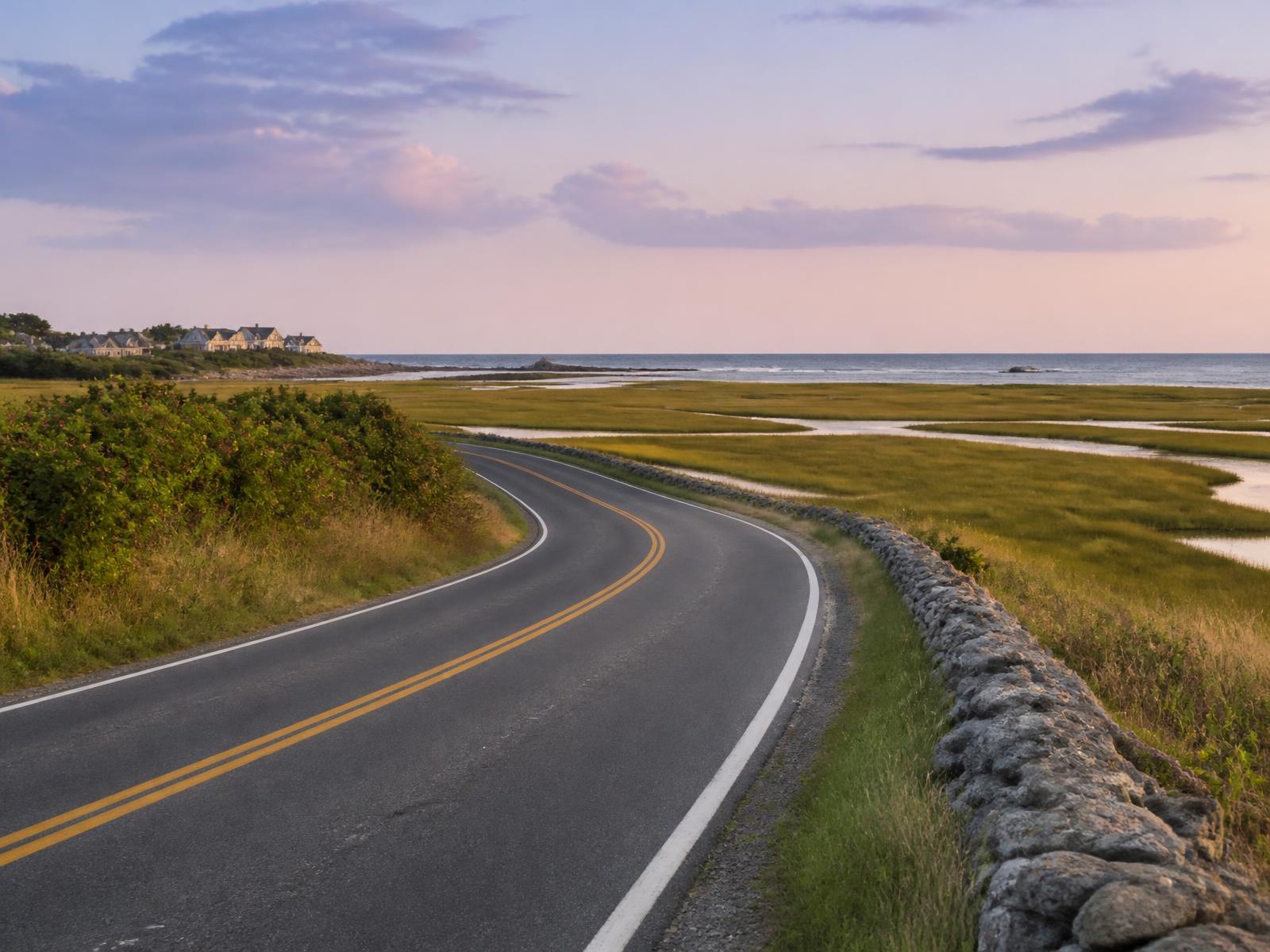 A quiet Seacoast road curving toward the water past salt marsh and a granite stone wall.